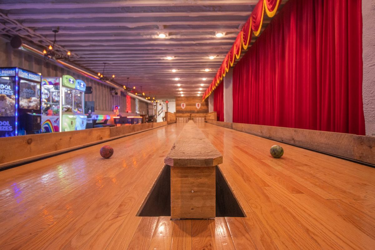 Two wooden candlepin bowling lanes under red curtains, with arcade machines along the left wall