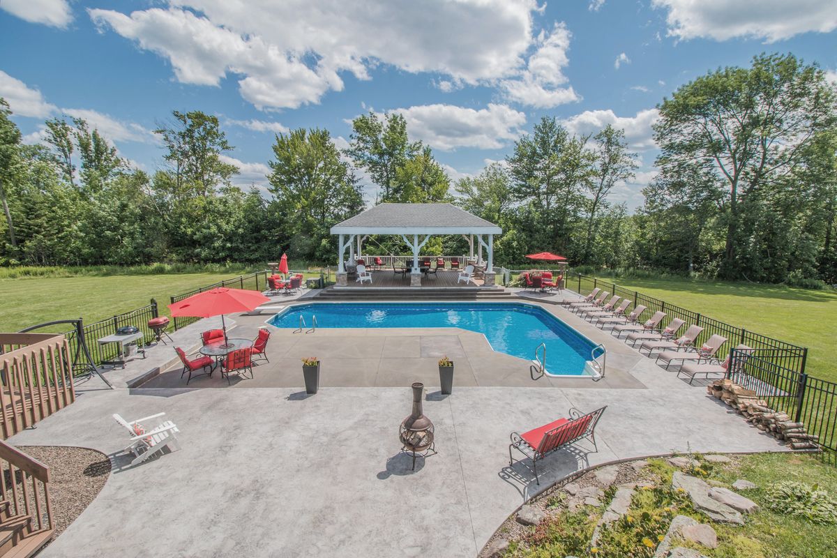 The Mansion's outdoor pool on a wide stone patio, red umbrellas and loungers around it and a white gazebo beyond