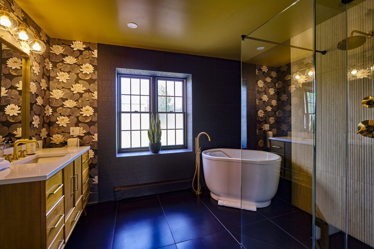 A bathroom with a freestanding soaking tub, gold fittings and patterned wallpaper